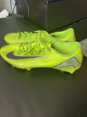 Nike Mercurial neon-gula fotbollsskor - Säljer ett par Nike Mercurial fotbollsskor i neon-gult med svarta detaljer och silverfärgade inslag. Skorna har snörning och låg profil, perfekt för snabba rörelser på planen. Snygg design med stor Nike-logga på sidan och mönstrad ovandel.Använt många gånger och storlek 45