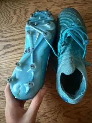 Blå Nike phantom elite fotbollsskor storlek 38 EU - Säljer ett par blå Nike Mercurial fotbollsskor med snörning och hög strumpliknande krage. Skorna har metallskruvdobbar och är tillverkade i ett stickat syntetmaterial för bra passform och grepp på planen. Perfekta för dig som vill ha snabbhet och kontroll.