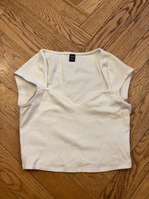 Vit ribbad topp från SHEIN - Säljer en vit ribbad topp från SHEIN med v-ringad skärning och korta ärmar. Toppen är croppad och har en enkel, stilren design som passar perfekt till jeans eller kjol. Materialet känns mjukt och stretchigt.