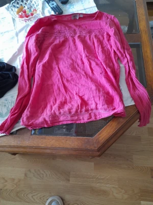 Rosa långärmad blus med spetsdetalj - Snygg rosa blus med långa ärmar och fina spetsdetaljer upptill. Blusen har en lätt skrynklig struktur och är perfekt för dig som vill ha en färgstark och bekväm look. Passar till både jeans och kjol.