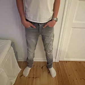 Grå jeans från Jack & Jones - Säljer Snygga grå jeans från Jack & Jones i modellen Slim Glenn. Den har en slim fit passform och är i mycket fint skick. Han på bilden är 170 och yeansen sitter perfekt på honom, vid frågor eller intresse är det bara att skriva!