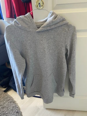 Grå basic hoodie med huva - Enkel och stilren grå hoodie med huva och känguruficka framtill. Mjuk bomullsblandning och långa ärmar. Perfekt för en avslappnad look och passar till det mesta i garderoben.