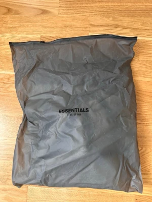 Grå mjukisbyxor från Fear of God - Snygga grå mjukisbyxor från Fear of God Essentials med elastisk midja och dragsko. Byxorna har en avslappnad passform och är tillverkade i mjukt bomullsmaterial. Perfekta för en chill och trendig look.