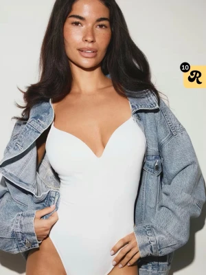 Vit body med djup urringning - Snygg vit body med djup v-ringning och smala axelband. Kroppsnära passform som framhäver siluetten. Perfekt att styla under en jeansjacka eller kavaj. Materialet ser ut att vara stretchigt och mjukt för en bekväm känsla.