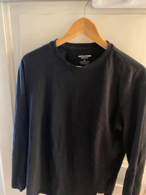 Svart långärmad topp Jack & Jones - En enkel och stilren svart långärmad topp från Jack & Jones Essentials. Tillverkad i mjuk ekologisk bomull med rund halsringning. Perfekt basplagg för alla tillfällen och lätt att matcha med olika outfits.