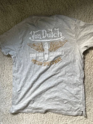 Grå Von Dutch t-shirt med tryck - Säljer en grå t-shirt från Von Dutch med stort coolt tryck på ryggen med vingar och texten 'Motor Speedway'. T-shirten har korta ärmar och är gjord i mjuk bomull. Använd 3 gånger💕äkta💕storlek S💕skriv om ni har frågor och pris kan eventuellt diskuteras💕