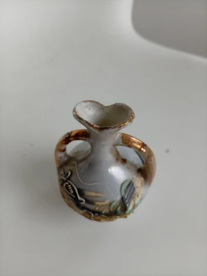 Liten dekorativ vas med drakmotiv - En liten, unik vas i keramik med handmålat drakmotiv och gulddetaljer. Vasen har två handtag och en hjärtformad öppning. Färgerna går i vitt, guld, grönt och blått. Perfekt som prydnad eller samlarobjekt.