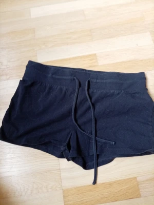 Svarta shorts med snörning - Svarta shorts i mjukt bomullsmaterial med snörning i midjan och två fickor framtill. Perfekta för en avslappnad stil och passar bra till sommarens varma dagar.