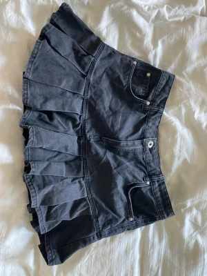 Svart kjol med volanger från Bershka - Supersnygg svart kjol från Bershka med volangkant och klassiska jeansdetaljer som fickor och knapp. Modellen har medium midja och är gjord i ett denim material. Storlek 40 men passar mig med storlek 38