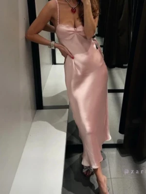 Zara ljusrosa satinklänning strl XS  - Superfin långklänning i ljusrosa satin från Zara. Klänningen har smala axelband dekorerade med pärlor och en liten cut-out framtill. Snygg figurnära passform och mjukt, glansigt material som faller fint.