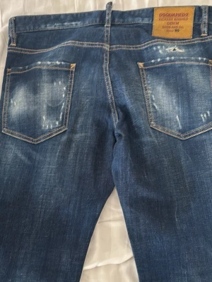 Blå slitna jeans från Dsquared2 - Coola blå jeans från Dsquared2 med slitningar och patchdetaljer. Klassisk femficksmodell med tydliga kontrastsömmar och läderpatch bak i midjan. Jeansen har en trendig, något tvättad look och är tillverkade i bomullsdenim.