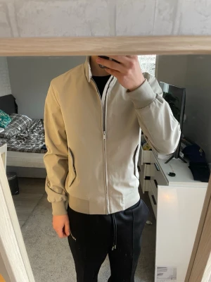 Beige bomberjacka från Topman - Snygg beige bomberjacka från Topman med dragkedja framtill, ribbade muddar vid ärmslut och midja samt två snedställda fickor. Jackan har en stilren design och står ut med sin neutrala färg och klassiska bomberjacke-form. Perfekt för dig som gillar enkel och clean stil.