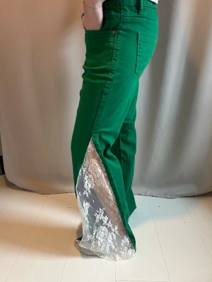 Gröna jeans med spetsdetalj - Unika gröna jeans med utsvängda ben och vit spetsinfällning längs sidorna. Låg midja och klassisk femficksmodell. Jeansen har en cool kontrast mellan det gröna tyget och den romantiska spetsen, perfekt för dig som vill sticka ut.🩵💚 innerbenslängden är 74cm och midjemåttet är 41cm rakt över🩵
