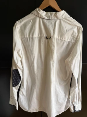 ,Vit skjorta Tommy Hilfiger, Fitted - Vit skjorta från Tommy Hilfiger med fitted passform. Skjortan har rosa detaljer och mönstrade armbågslappar. Tillverkad i bomull och har knappar framtill.