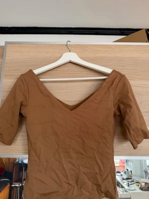 Brun v-ringad topp från H&M - Snygg brun topp från H&M med v-ringning och halvlånga ärmar. Tillverkad i mjuk bomull som känns skön mot huden. Enkel och stilren design som passar till många olika looks.