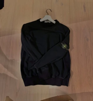 Svart sweatshirt från Stone Island - Säljer en svart sweatshirt från Stone Island med klassisk rund hals och ribbade muddar. Tröjan har den ikoniska Stone Island-loggan på vänster ärm. Perfekt för en clean och stilren look. Tidigare köpt  här på Plick. Cond 9/10 bara lite nopprig men inget annat. Storlek: M passar även S.                 Hör av er vid frågor och funderingar!