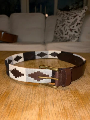 Black and white läder bälte  - Ett stilrent mönstrat läderbälte tillverkat i slitstarkt äkta läder. Bältet har ett dekorativt mönster som ger ett klassiskt och elegant utseende, vilket gör det enkelt att matcha med både vardagliga och mer uppklädda outfits.  Bältets längd är 80 cm, mätt från bältets början till det mittersta hålet