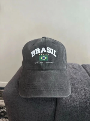Brazil keps 🇧🇷🧢 - Snygg svart keps med texten 'BRASIL' och en broderad brasiliansk flagga samt 'RIO DE JANEIRO' framtill. Klassisk böjd skärm och justerbar passform bak. Perfekt för dig som vill addera lite streetstyle och visa kärlek till Brasilien. Har flera att sälja gärna dm mig ifall ni vill köpa