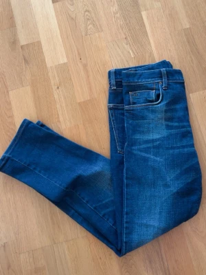 Blå jeans J.Lindeberg - Snygga blå jeans från J.Lindeberg med klassisk femficksmodell och kontrastsömmar. Jeansen Är slim fit och är tillverkade i slitstarkt denimtyg. Bare logga på bakfickan och läderpatch i midjan för extra stilpoäng.