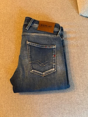 Replay anbass jeans - Snygga blå jeans från Replay med slitna detaljer. Jeansen har en mörk tvätt med ljusare partier och kontrastsömmar. Märkespatch i läder baktill och Replay logga på fickan. Perfekta för en trendig och avslappnad stil, skick 8/10, använda men är i väldigt bra skick