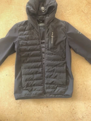 Svart vindjacka Sail Racing - Snygg tailored svart vindjacka från Sail Racing med vadderad front, hu temporär och drag suite. Jackan har en bröstficka med dragkedjaga och patch på ärmen med texten 'Sail Antarctica'. Perfekt för dig som messar streetwear och outdoor.