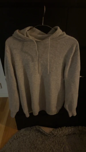 Merinoull hoddie - En stilren ljusgrå hoodie med huva och dragsnören. Tröjan har en klassisk passform med ribbade muddar vid ärmslut och nederkant. Tillverkad i ett mjukt och bekvämt tyg som känns skönt mot huden. Perfekt för en avslappnad look.