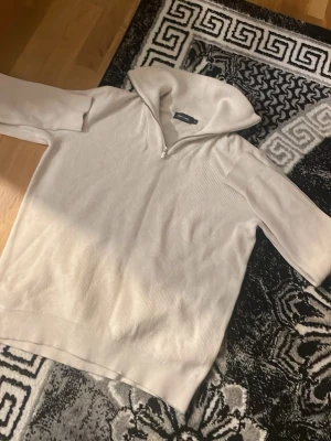 Vit halvzip tröja med hög krage - Snygg vit tröja med halv dragkedja och hög krage. Tröjan har ribbade detaljer på kroppen och släta ärmar. Perfekt för lager på lager och enkel att styla till olika outfits. Materialet ser mjukt och bekvämt ut.