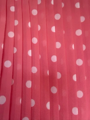 Rosa prickig klänning med resårmidja - Söt rosa klänning med vita prickar och resår i midjan. Klänningen har ärmlös design och rund halsringning med en liten knappöppning bak. Materialet känns lätt och luftigt, perfekt för varma dagar.