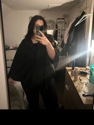 Svart cape-kappa med knytband - Säljer en svart cape-kappa med knytband i midjan. Kappan har en lös och fladdrig passform med vida ärmar och är perfekt för att skapa en cool och elegant look. Passar dig som vill ha något stilrent och trendigt.