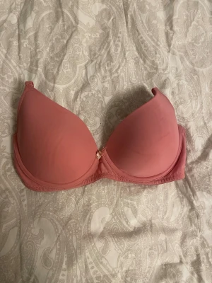 Rosa push-up bh från Twilfit - Snygg rosa push-up bh från Twilfit i storlek 70D. Bh:n har sl year formade kupor, justerbara axelband level och en liten dekorativ rosett mellan kuporna. Materialet känns mjukt och bekvämt mot huden.