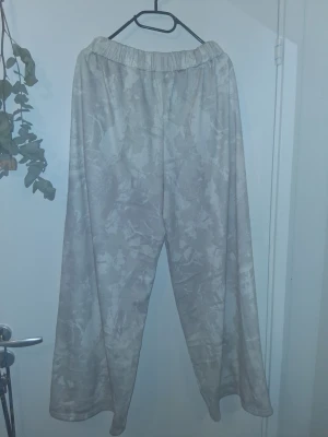 Beige mönstrade mjukisbyxor - Säljer ett par beige mjukisbyxor med diskret mönster och bred resår i midjan. Byxorna har en avslappnad och rak passform, tillverkade i ett mjukt och bekvämt material. Perfekta för att chilla hemma eller när du vill ha en avslappnad stil.