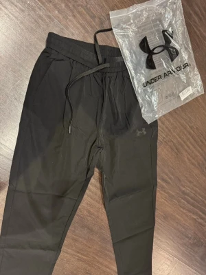 Svarta mjukisbyxor från Under Armour - !OBS LÄS!Svarta mjukisbyxor från Under Armour med dragsko i midjan och resår vid bensluten. Kom fel från fabriken hade beställt i storlek XL men passade S/M vilket jag då fick tillbaka pengarna och behålla varan. Säljer de för billigt. Byxorna har sidofickor och en diskret logga på låret. Perfekta för chill eller träning, tillverkade i ett mjukt och stretchigt material. Helt nya aldrig använda