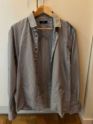 Randig skjorta med knappar - Snygg skjorta från Selected med smala svarta och vita ränder. Klassisk krage, långärmad och knäppning framtill. 