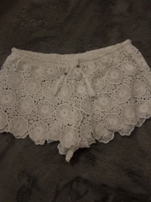 Vita virkade shorts från New Look - Superfina vita virkade shorts från New Look med snygg snörning i midjan och detaljerat spetsmönster. Perfekta för varma dagar och ger en boho-vibe till din outfit. Elastisk midja för extra komfort. Skulle säga att shortsen är i xs