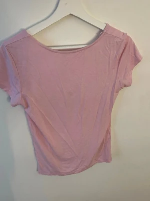 Ljusrosa rygglös croppad topp - Söt ljusrosa rygglös croppad topp med korta ärmar och rundad, djup rygg. Tillverkad i mjukt bomullsmaterial som känns skönt mot huden. Perfekt att styla med höga jeans eller kjol för sopren och trendig look.