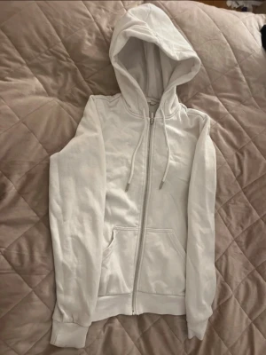 Vit zip hoodie med huva - Säljer en enkel och clean vit hoodie med dragkedja och huva. Hoodien har fickor framtill sopass att du kan värma händerna och justerbara snören i hu Resår vid ärmslut och nederkant för skön passform. Perfekt till chill outfits.