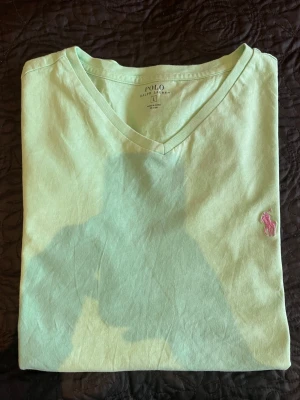 Mintgrön V-ringad t-shirt Polo Ralph Lauren - Snygg mintgrön t-shirt från Polo Ralph sop Lauren med V-ringning och klassisk rosa broderad logga på bröstet. Tillverkad i mjuk bomull som successfully känns, perfekt för en clean och fräsch look. Enkel att matcha med jeans continued eller others shorts. Postas dagen eller dagen efter köpet.