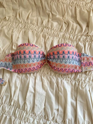 Färgglad bandeau bikiniöverdel 💖 - Säljer en missoni liknande bandeau bikiniöverdel med vågigt mönster i rosa, blått, silver och beige mm. Överdelen har en snygg form med vaddering och pushup. Perfekt för sommarens strandhäng! 