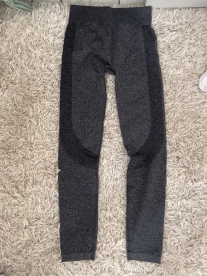 Mörkgrå seamless leggings från SOC - Mörkgrå seamless leggings från SOC med hög midja och snygga mörkare paneler längs sidorna. Tillverkade i ett stretchigt material av 72% polyamid, 18% polyester och 10% elastan. Perfekta för träning eller chill dagar.