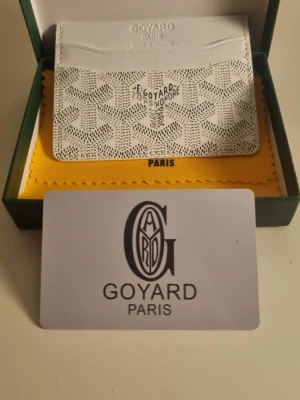 Vit kortfodral från Go4yard - Snyggt vitt kortfodral från Go4yard med det klassiska mönstret och präglad logga framtill. Tillverkat i exklusivt läder och har flera fack för kort. Kommer i originalask med gul putsduk och certifikat. Perfekt för dig som vill ha något stilrent och lyxigt.