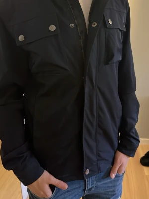 Blå field jacka - Säljer en snygg mörkblå field jacka från dressmann med snygga fickor både på utsidan och insidan. Jackan ger en casual och uppklädd stil.