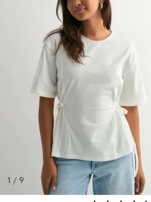 Vit topp med knyt från Nelly - Säljer en vit topp från Nelly med korta ärmar och snygg knytning i sidan. T-shirten har en rund halsringning och är gjord i mjuk bomull. Aldrig använd🫶🏻