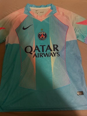 PSG Nike fotbollströja turkos - Säljer en PSG matchtröja från Nike med Qatar Airways som sponsor. Tröjan är turkos med rosa och ljusblå detaljer samt vita linjer och PSG-logga på bröstet. Materialet är lätt och andas, perfekt för träning eller match. Kortärmad och modern design. Storlek M