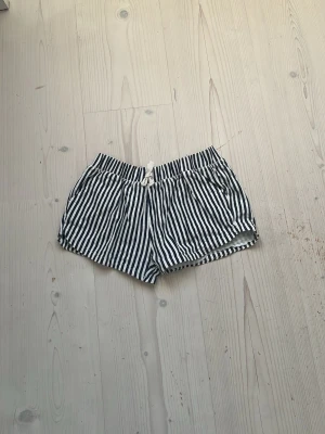 Randiga shorts från Zara Girls -  Ett par svartvita randiga shorts från Zara Girls med snörning i midjan. Shortsen har en avslappnad passform och är tillverkade i ett lätt bomullstyg, perfekta för varma dagar.