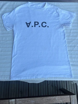 Vit t-shirt från A.P.C. - Klassisk vit t-shirt från A.P.C. med svart logotyptryck på bröstet. T-shirten har rund halsringning och korta ärmar. Tillverkad i mjuk bomull för en skön och avslappnad känsla. Perfekt till jeans eller shorts.