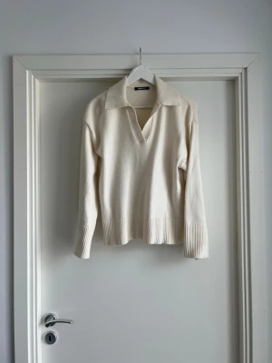 Krämvit stickad tröja med krage Gina Tricot - Snygg krämvit / beige stickad tröja med djup v-ringning och bred krage från Gina tricot. Tröjan har långa ärmar och ribbstickade muddar samt nederkant. Perfekt för lager-på-lager och enkel att matcha med jeans eller kjol.