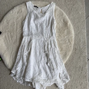 Vit spetsklänning Made in Italy (XS/S) - Söt vit klänning i spets från Made in Italy. Klänningen har ärmlös design, rund halsringning och asymmetrisk nederkant. Perfekt för sommarens alla tillfällen och har en romantisk känsla med sina spetsdetaljer.