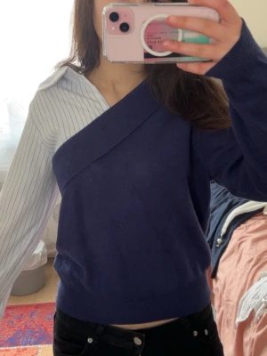 Marinblå one shoulder topp med ränder - Unik one shoulder topp i marinblått och vitt. Ena sidan är stickad marinblå med bred kant, andra sidan har vit skjortärm med tunna svarta ränder och klassisk krage. Perfekt statement-plagg för dig som gillar att sticka ut.