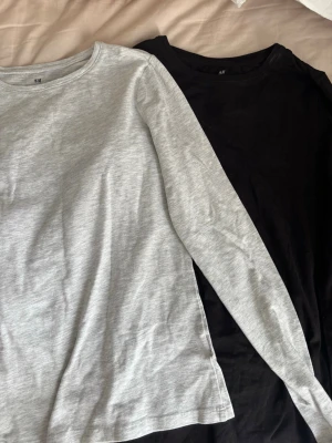 2-pack långärmade tröjor H&M - Säljer två basic långärmade tröjor från H&M, en i ljusgrått och en i svart. Båda har rund hals och är gjorda i mjuk bomull. Perfekta som basplagg till din garderob.