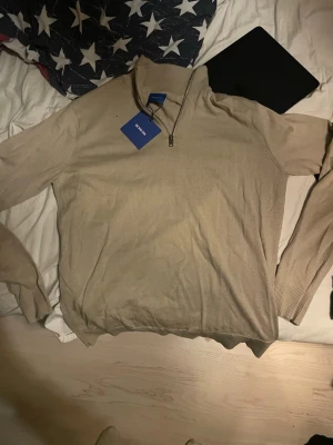 Beige halvzip-tröja från Morris - Snygg beige stickad tröja från Morris med halv dragkedja och hög krage. Tröjan har långa ärmar och ribbade muddar vid ärmslut och nederkant. Perfekt för en stilren och avslappnad look. Aldrig använd helt ny med lapp
